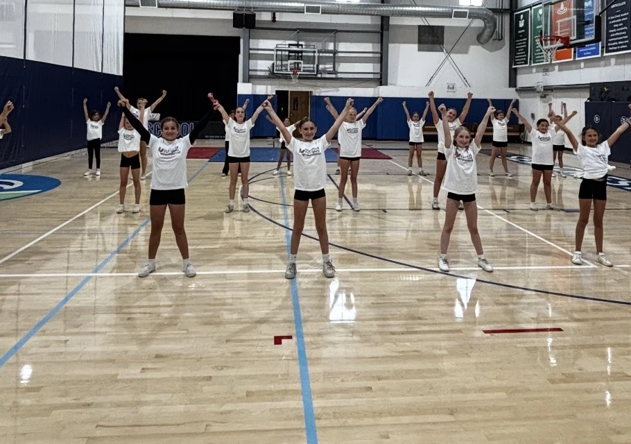 Girls cheerleading with arms raised in Stanford Park Sports Foundation shirts at summer camp