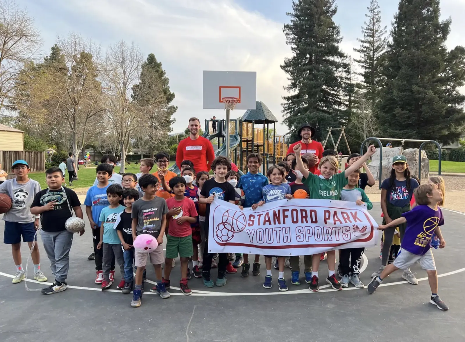 Large group of students holding a Stanford Park Youth Sports banner on a school court