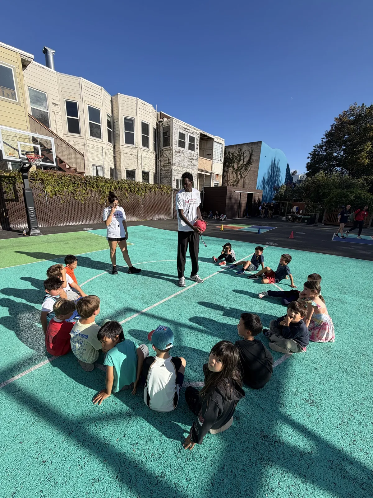 Students gathered around their coach on a bright teal outdoor court