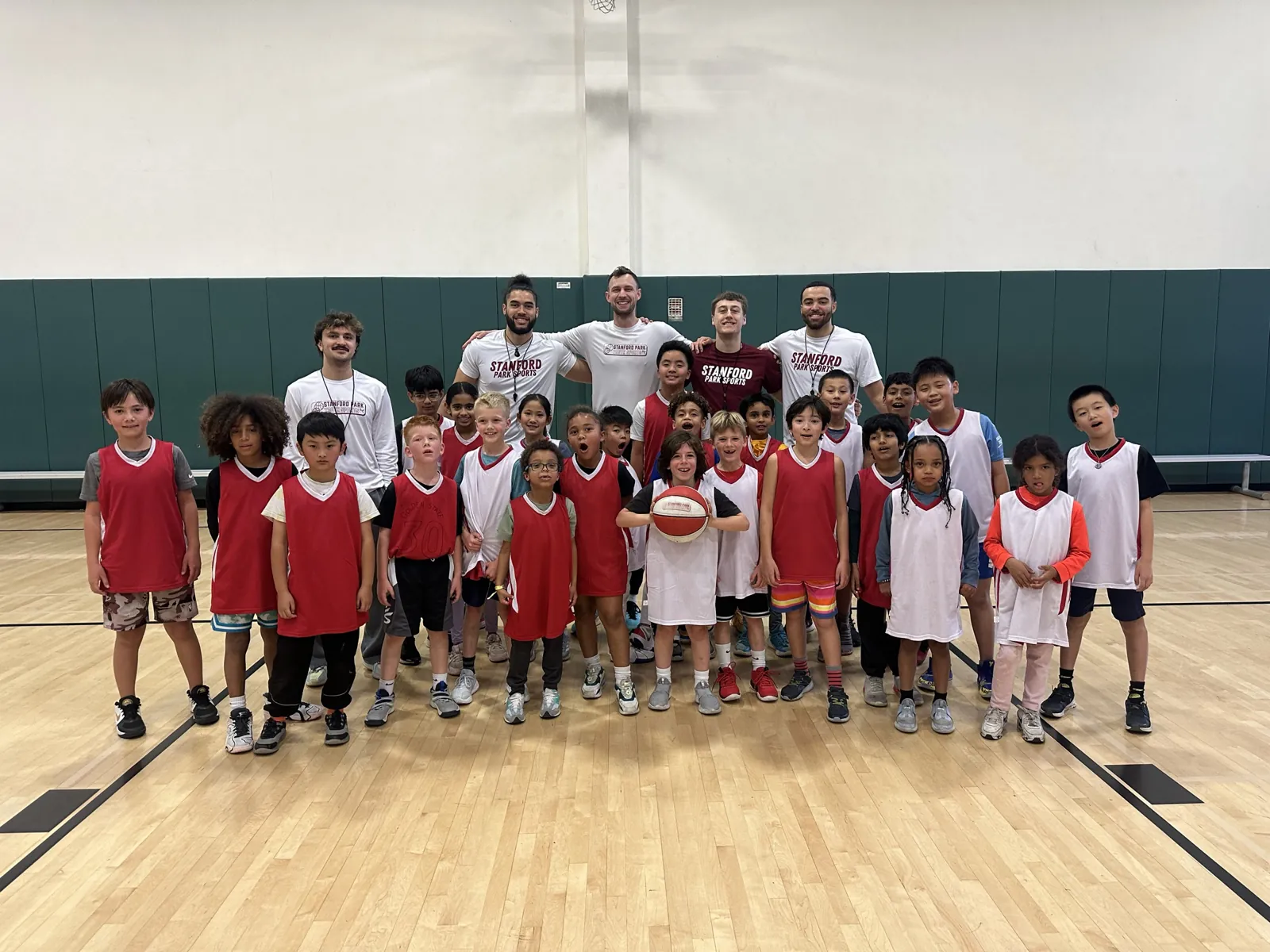 Large camp group in red and white jerseys with four Stanford Park Sports coaches in a gym
