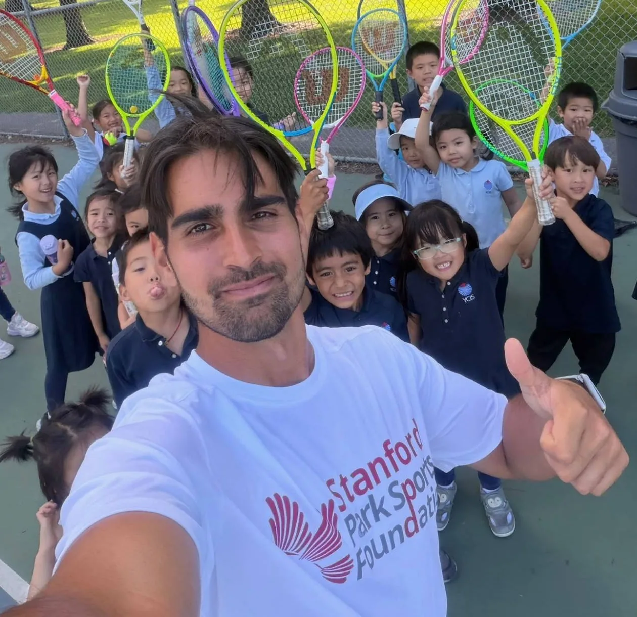 Stanford Park Sports coach taking a selfie with uniformed students holding up tennis rackets during PE